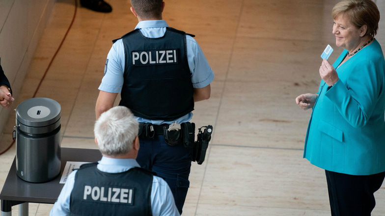 Bundeskanzlerin Angela Merkel steht neben Polizeibeamten im Bundestag.
