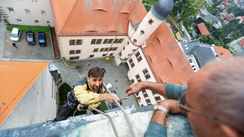 Tobias Vogler hängt am Kirchturm über den Dächern von Dippoldiswalde. Kirchner Andreas Kunath reicht ihm Werkzeug, das für einen Uhrmacher riesig ist.