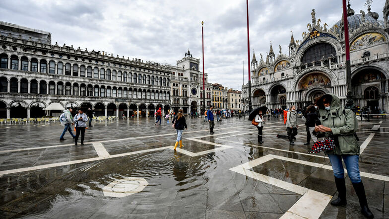 Passanten gehen bei Regen über den überschwemmten Markusplatz in Venedig. Ein Unwetter mit Regen und Sturm hat im Norden des Landes heftige Schäden angerichtet.
