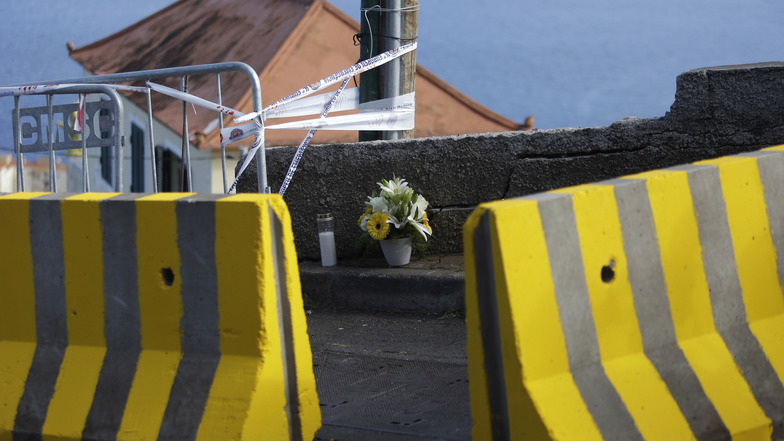 Blumen und eine Kerze stehen am Straßenrand hinter Betonschutzwänden, an der Unfallstelle des Busunglücks.