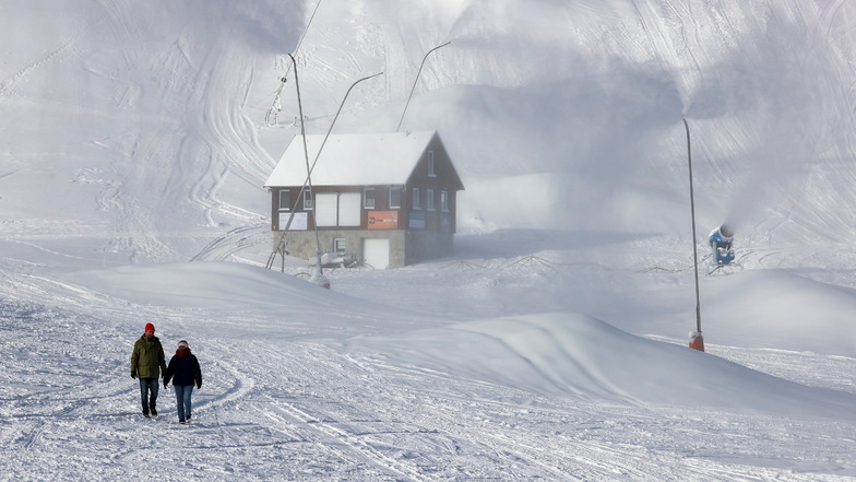 Zwei Spaziergänger gehen über die leere Skipiste auf dem Fichtelberg. Am Wochenende soll hier der Skibetrieb unter 2G ermöglicht werden.