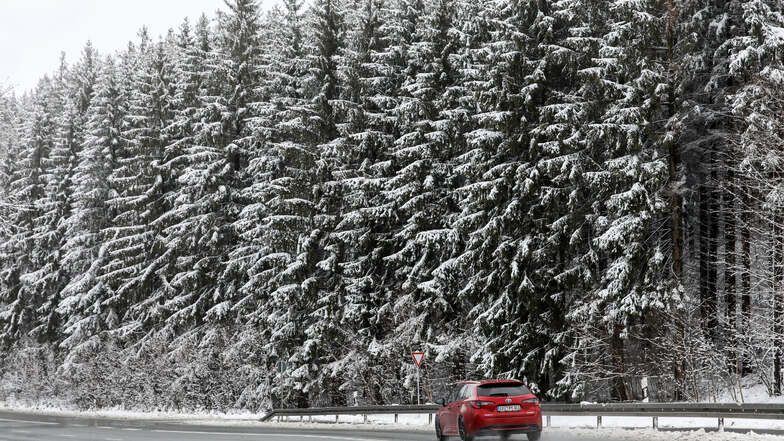 in Auto fährt auf einer Landstraße durch den verschneiten Wald bei Einsiedel. 