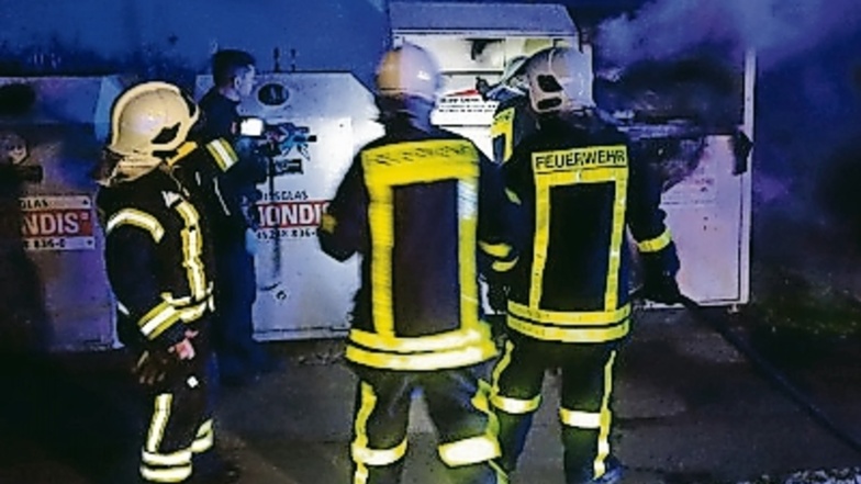 Die Großenhainer Feuerwehrleute haben den brennenden Altkleidercontainer mit dem Schnelleinsatzschlauch gelöscht, sodass er nur noch qualmt.