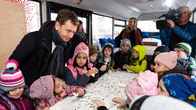 Michael Kretschmer (l, CDU), Ministerpräsident von Sachsen, spricht bei der Auftaktveranstaltung zur Museumsbus-Tour der Staatlichen Kunstsammlungen Dresden mit Kindern im mobilen Museum in einem Bus.