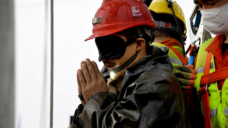 Ein Bergmann mit Augenmaske legt im Ausdruck seiner Dankbarkeit die Hände aneinander, nachdem er aus der Mine geborgen wurde.