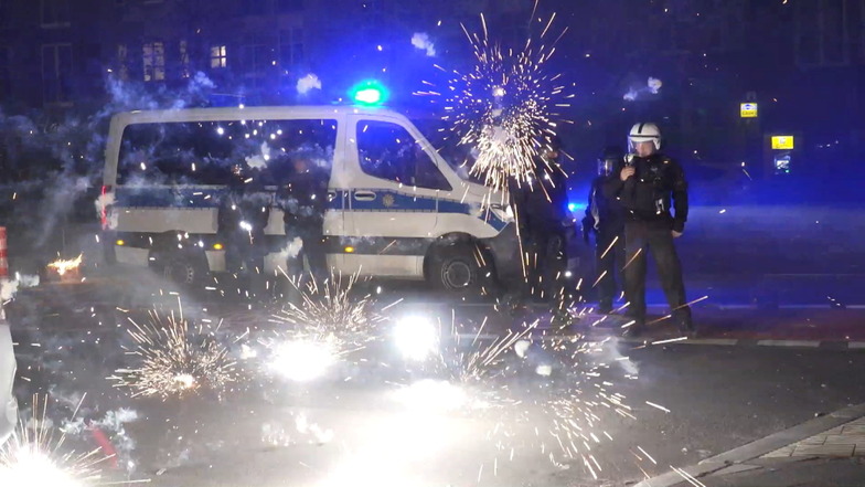 Berliner Polizisten stehen hinter explodierendem Feuerwerk. Nach Angriffen auf Einsatzkräfte in der Silvesternacht hat die Diskussion um Konsequenzen auch in Dresden begonnen.