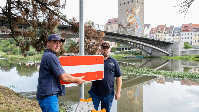 Jens Franze (links) und Mirko Kober befestigen ein Schild vor der Altstadtbrücke in Görlitz. Damit wird angezeigt, dass die Bootsfahrt über das nahe Wehr verboten ist.