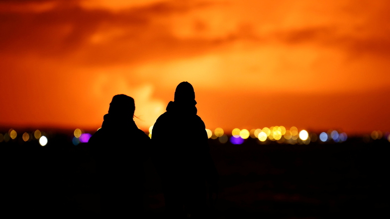 Menschen beobachten, wie der Nachthimmel nach dem Ausbruch des Vulkans von der Hauptstadt Reykjavik aus gesehen erhellt wird.