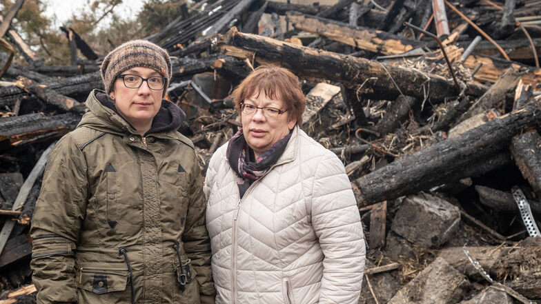 Sabina Saafi (l.) und Karla Lügner stehen vor den Resten der Scheune, die in der Nacht zum Freitag in Großharthau niederbrannte. Wegen der Spurensicherung durch die Polizei werden sie den Schutt nur schichtweise abtragen können.