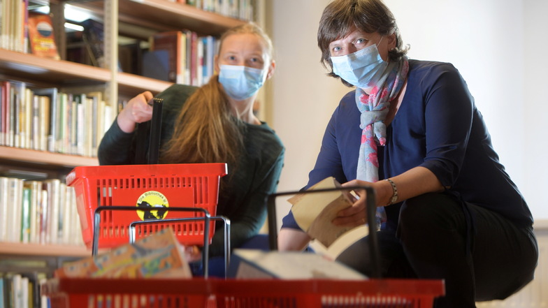 Viktoria Stabrey und  Carola Becker (r.) füllen die Körbe mit den bestellten Büchern und Spielen in der Christian-Weise-Bibliothek in Zittau.