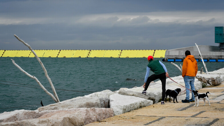 Zwei Passanten stehen am Wasser während die neue Hochwasserschutzanlage Mose vor Venedig erstmals zum Schutz vor Hochwasser hochgefahren wird.