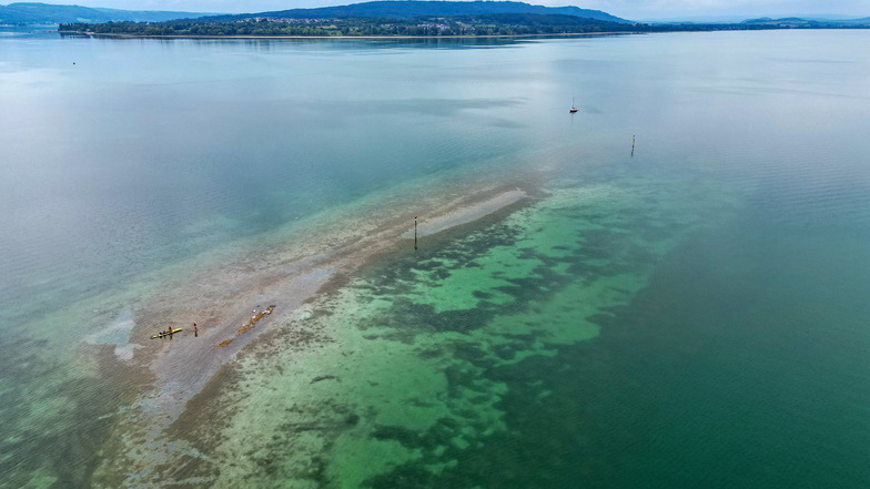 Durch das Niedrigwasser des Bodensees ist zwischen der Halbinsel Mettnau und der Insel Reichenau im Bodensee eine Kiesbank zu sehen. Zwei Kanufahrer legen gerade dort an, im Hintergrund die Halbinsel Höri.