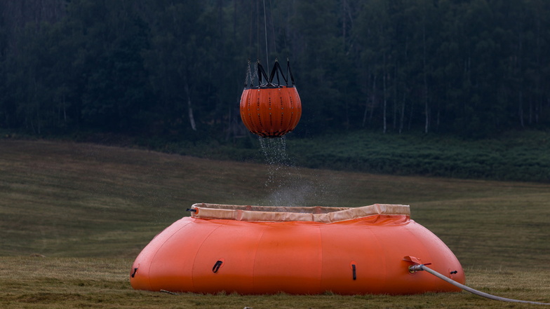 Ein Hubschrauber schöpft Wasser aus einem Faltbehälter.