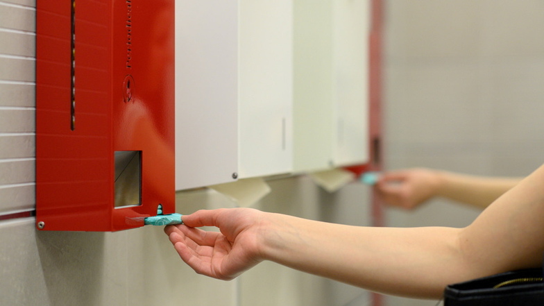 Ein Frau zieht in einer Damentoilette  eine Binde aus einem Tampon- und Bindenspender: Solche  Automaten könnten in Mädchentoiletten von Schulen in Sachsen bald alltäglich sein.