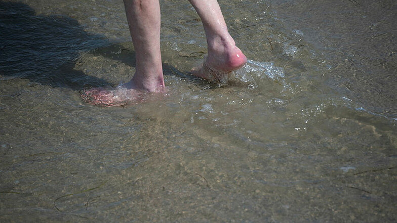 Ein Mann watet durch das flache Wasser am Strand der Ostsee. In Mecklenburg-Vorpommern wurden die ersten Vibrionen-Todesfälle in diesem Jahr registriert.