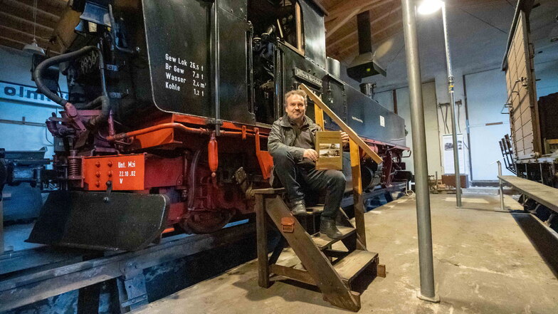 Museumsleiter Peter Wunderwald sitzt an einer alten Dampflok. In seinen Händen hält er ein Buch über das Schienenstreckennetz in Freital.
