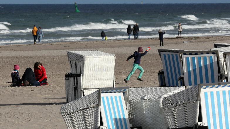 Am Ostseestrand von Warnemünde  sind Strandbesucher spazieren und lassen Drachen steigen.