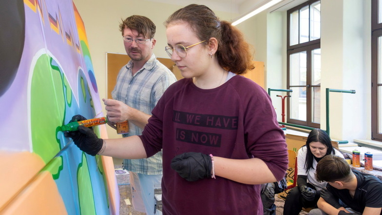 Emily Franke zieht die Konturen auf dem Bild nach, das die Klasse 8a gemeinsam mit Graffiti-Künstler Carsten Langner (l.) gestaltet hatte.