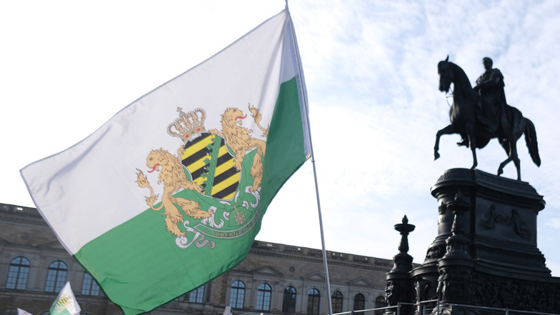 Teilnehmer einer Demonstration versammeln sich mit Transparenten und Fahnen auf dem Dresdner Theaterplatz, darunter die Fahne, die von der rechten Kleinpartei „Freie Sachsen“ genutzt wird.