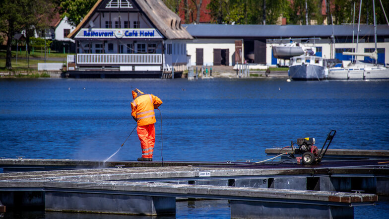 Mit einem Hochdruckreiniger putzt ein Mann einen leeren Bootssteg im Stadthafen an der Müritz. Die Tourismusbetriebe an der Mecklenburgischen Seenplatte bereiteten sich auf Corona-Lockerungen vor.