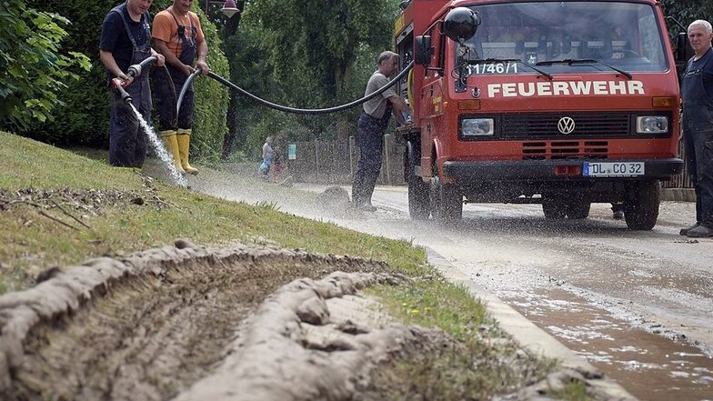 Aufräumen in Pulsitz: Schrebitzer Feuerwehrleute spülen den Schlamm von der Straße, den der heftige Regenguss von den Feldern gespült hat.