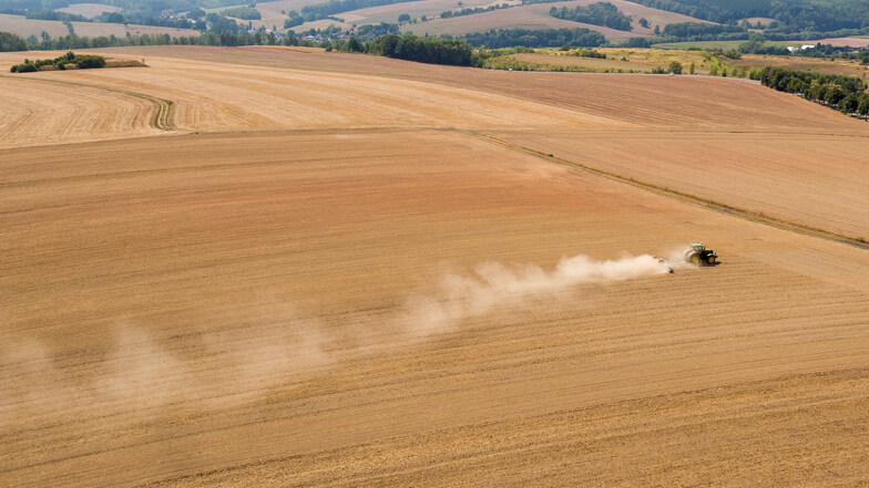 Sachsen, St. Egidien: Ein Traktor wirbelt Staub bei der Feldarbeit auf einem trockenen Feld auf.
