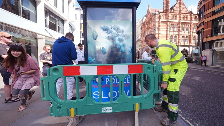 Ein neues Kunstwerk von Banksy mit schwimmenden Fischen, das auf einem Polizeikasten in der Londoner Innenstadt erschienen ist, wird von Arbeitern abgesperrt.