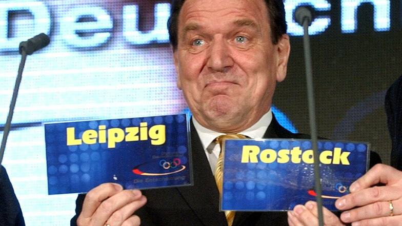 Bundeskanzler Gerhard Schröder präsentiert die Siegerstädte – und schaut dabei überrascht. In Rostock sollten die Segelwettbewerbe ausgetragen werden.
