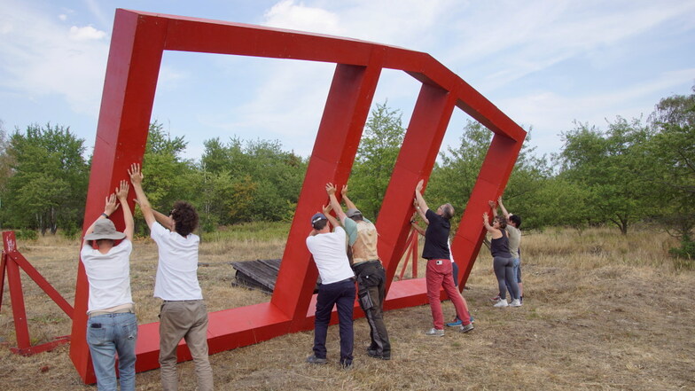 Mitglieder eines internationalen Jugendcamps stellen den roten Giebel einer ehemaligen Gefängnisbaracke am Rande der Gohrischheide auf.