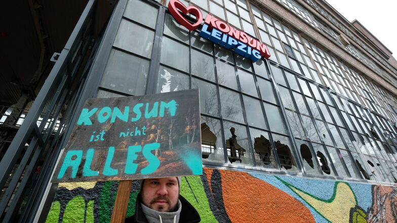 Ein Aktivist steht mit einem Schild mit der Aufschrift ·Konsum ist nicht alles· im Stadtteil Plagwitz vor dem Westwerk.