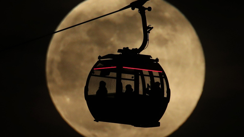 Eine Seilbahn fährt in London vor dem hellen Mond entlang. 