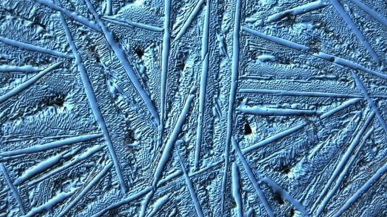 Erst unterm Mikroskop wird das sogenannte Ledeburit sichtbar. Es ist das, was zwischen den nadelförmigen Strukturen liegt. Der abgebildete Werkstoff ist Hartguss.