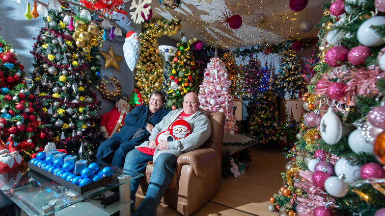 Susanne und Thomas Jeromin sitzen inmitten von Weihnachtsbäumen in ihrem Wohnzimmer. Sie halten den offiziellen Weltrekord für die "meisten geschmückten Weihnachtsbäume an einem Ort".