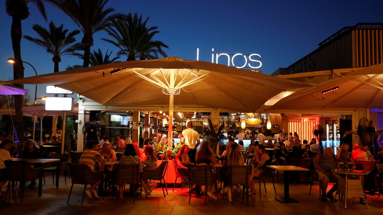 Menschen sitzen in einer Bar an der Strandpromenade von Palma.