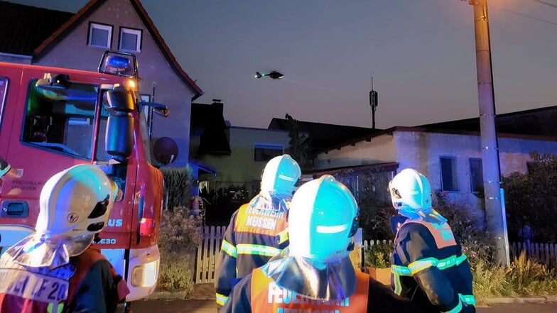 Einsatzkräfte der Freiwilligen Feuerwehr Meißen am Einsatzort in Altzaschendorf. Im Hintergrund ist ein Rettungshubschrauber im Anflug.