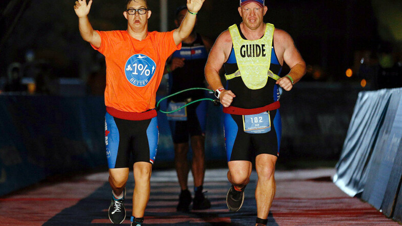 An der Seite seines Trainers Daniel Grieb läuft Chris Nikic (l) mit erhobenen Armen ins Ziel des Ironman Florida.