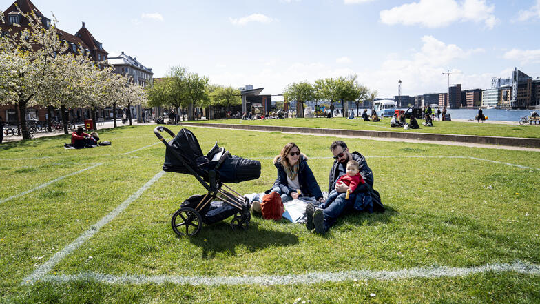 Eine Familie genießt die Sonne in Kopenhagen. Markierte Flächen auf dem Grasland helfen den Menschen, Abstand voneinander zu halten, wobei etwa 40 Quadratmeter Fläche für maximal 10 Personen markiert sind.