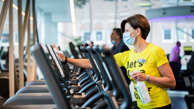 Eine Beschäftigte mit Atemschutz desinfiziert ein Laufband im Fitnessstudio.