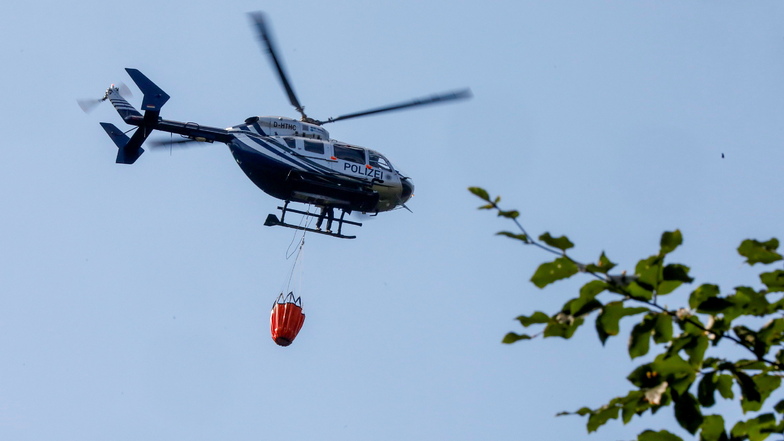 Bei einem Waldbrand in Sachsen kommt ein Polizeihubschrauber mit Wasser zu Hilfe.