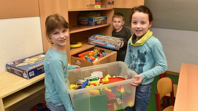Mia, Lena und Fynn haben damit begonnen, die Spiele aus dem Hort in einem Schrank im Kreativzimmer in der Schule einzuräumen.
