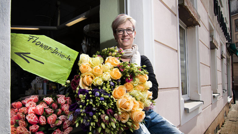 Nur für den Fotografen hat sich Ramona Holstein, Inhaberin des Blumen ABC, außen auf das Fensterbrett ihres Ladens gesetzt. Normalerweise steht sie im Laden und bedient die Kunden in einer Art Drive-In durch das Fenster.