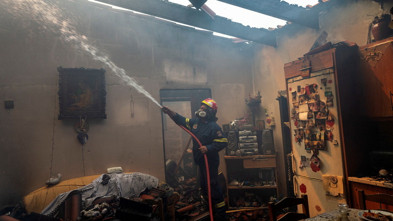 Ein Feuerwehrmann löscht ein Haus während eines Waldbrandes im Dorf Hasia in der Nähe von Athen.