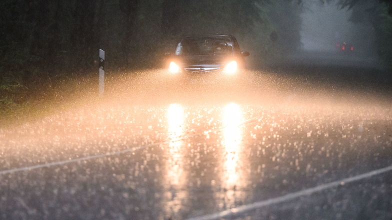 Ein Auto fährt während eines Gewitters mit Starkregen über eine Landstraße.