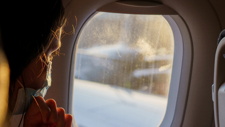 Ein weiblicher Fluggast mit Maske schaut vor dem Start eines Flugzeugs aus dem Fenster. Die Maskenpflicht beim Fliegen bleibt von und nach Deutschland.