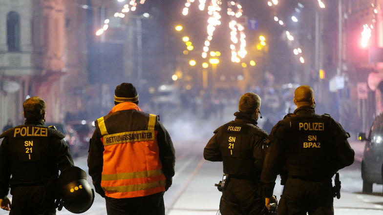 Polizisten und ein Rettungssanitäter stehen an einer Kreuzung in Leipzig. Die Stadt Leipzig hatte für die Silvesternacht Versammlungen verboten und in drei Zonen - darunter am Connewitzer Kreuz - ein Böllerverbot erlassen.