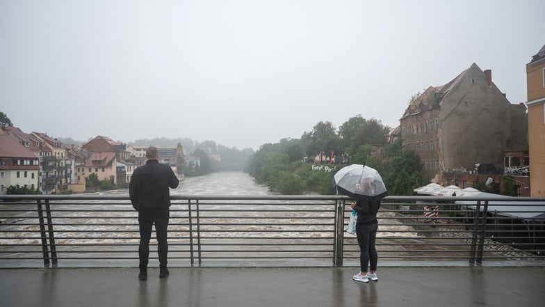 Zwei Passanten beobachten von der Altstadtbrücke in Görlitz aus die Hochwasser führende Neiße.