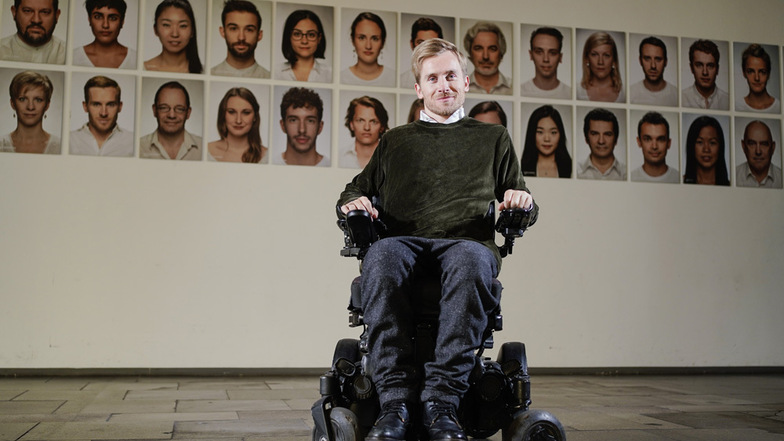Samuel Koch, festes Ensemblemitglied am Nationaltheater Mannheim, steht mit seinem Rollstuhl im Foyer des Nationaltheaters vor Bildern von Schauspieler-Kollegen.