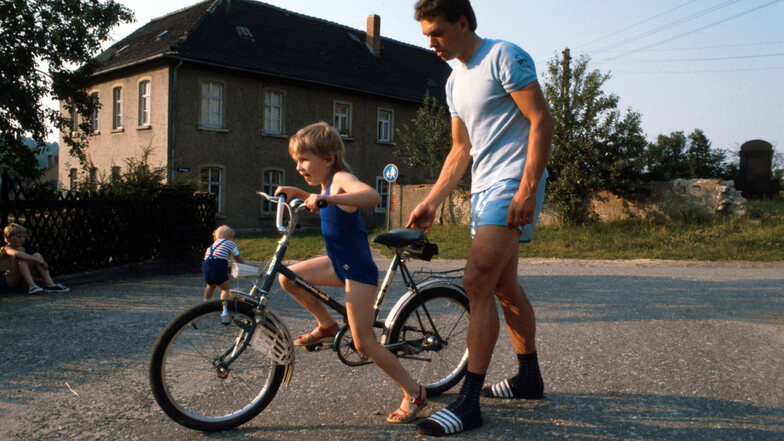 Mitte der Achtziger: Radrennfahrer Olaf Ludwig hilft Tochter Madlen beim Gleichgewichthalten. Er hat die DDR bewusst erlebt, sie nicht mehr. Viele jüngere Ostdeutsche wissen nichts über das Leben vor 1989. Das liegt oft an der Scheu vor dem Fragen.