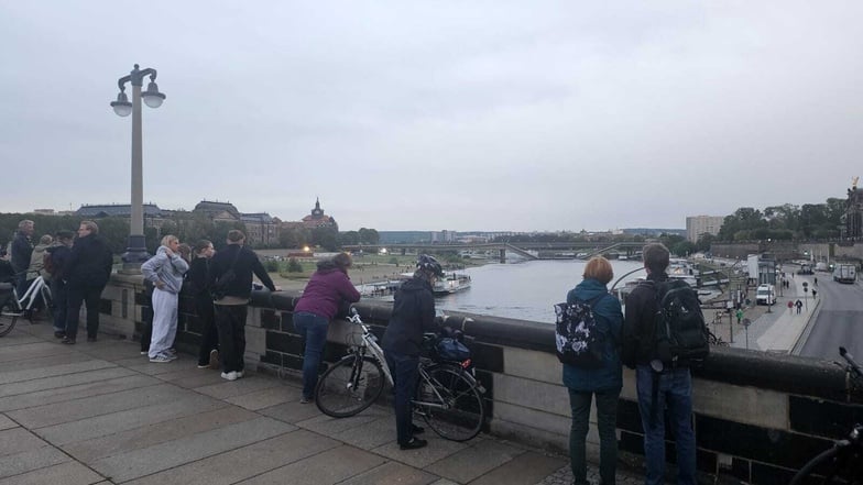 Zahlreiche Menschen stehen am Abend auf der Augustusbrücke und betrachten die eingestürzte Carolabrücke.