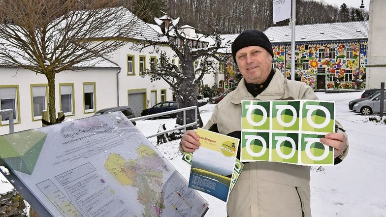Kreiswanderwegewart Gunter Fichte zeigt vor dem Geoparkzentrum Dorfhain das Logo des neuen Wanderweges.